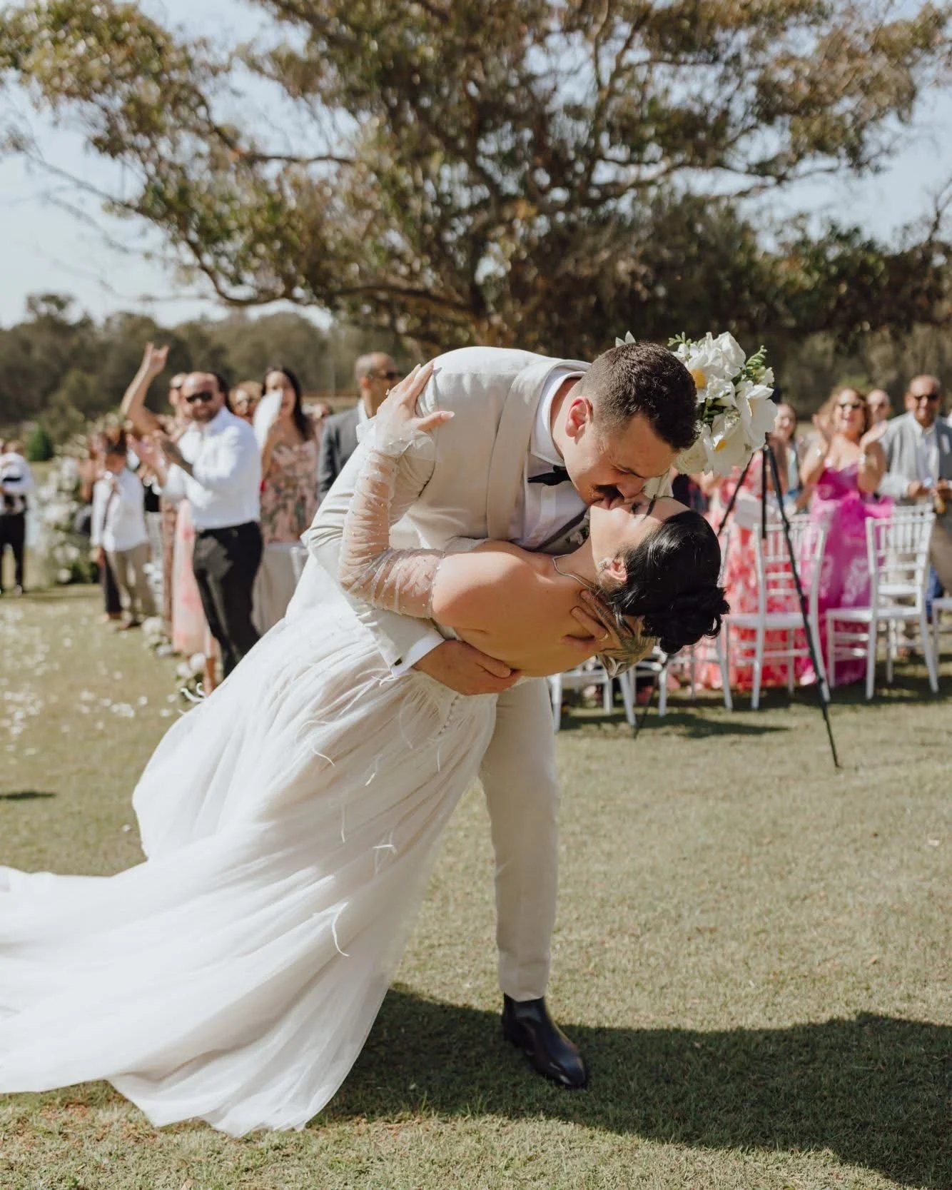 The groom dips the bride at the end of the aisle, guests clapping