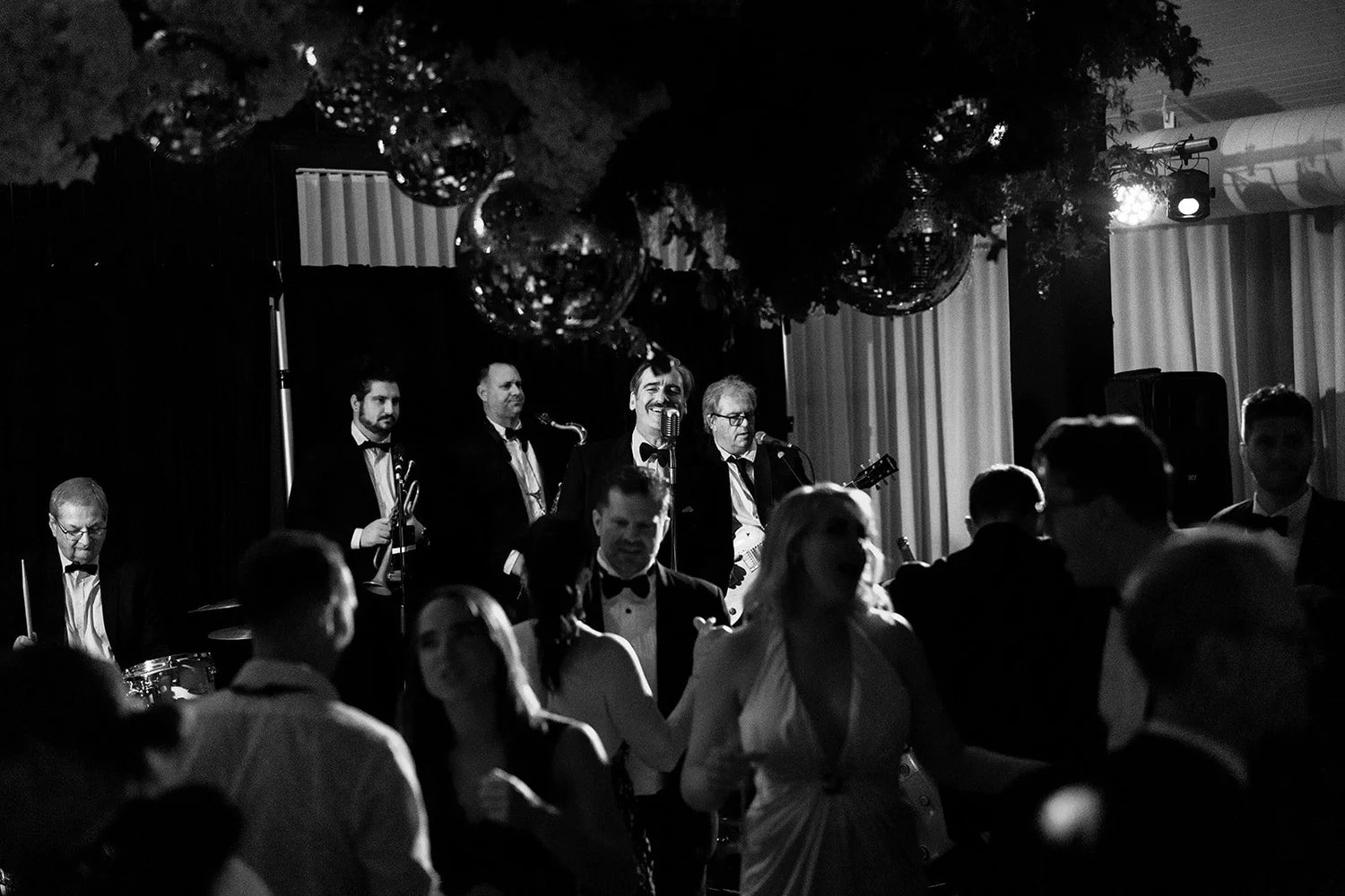 A packed dance floor under disco balls, in black and white