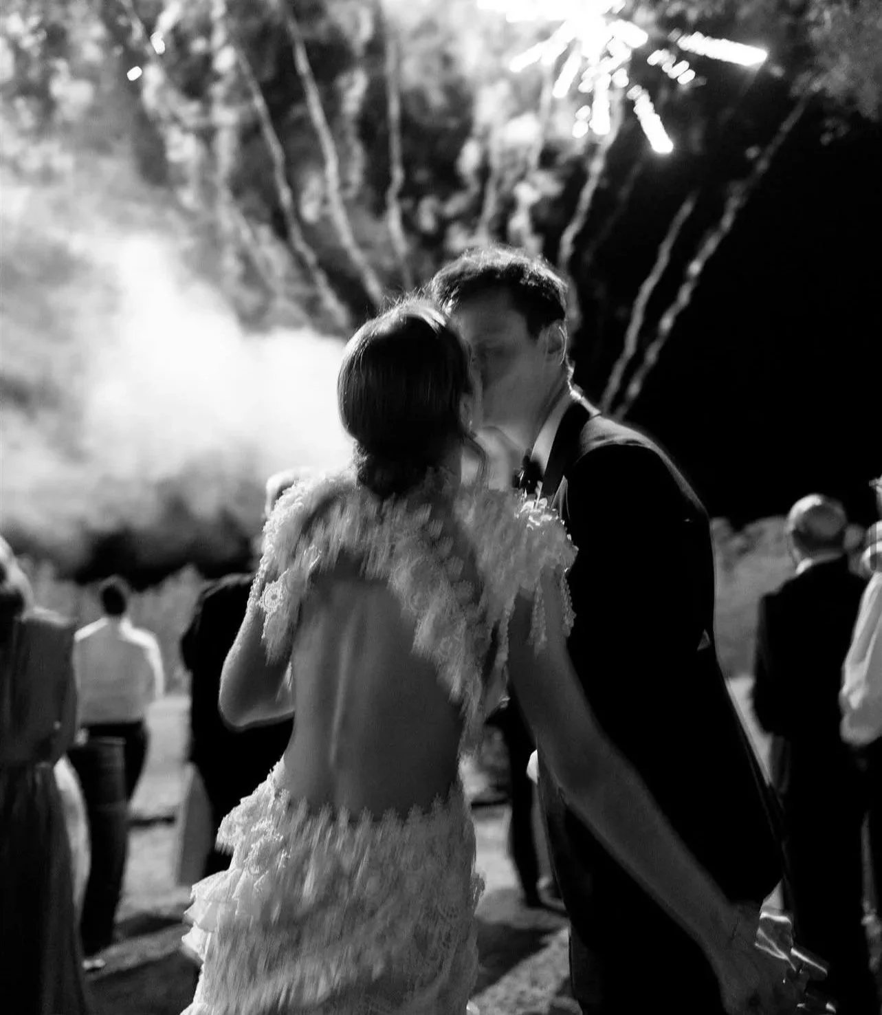 A kiss with fireworks and sparklers behind, in black and white